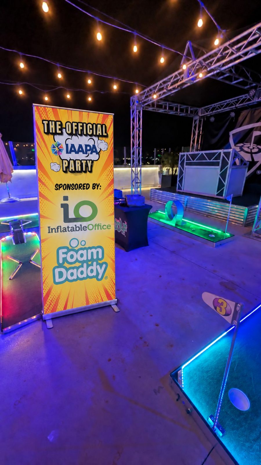 Official IAAPA Party banner sponsored by Inflatable Office and Foam Daddy beside the rooftop mini-golf course at night